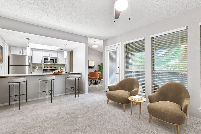 Modern open-concept living room with plush seating, large windows, and a sleek kitchen with bar seating.