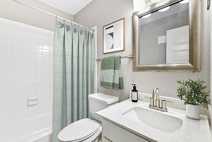 Modern bathroom with elegant fixtures, a large mirror, and stylish striped shower curtain. Features a sleek white sink and vibrant green accents for a fresh, inviting atmosphere.