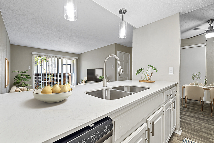 Contemporary open-concept kitchen and living area featuring sleek white countertops, modern pendant lighting, and a view of the cozy dining space.