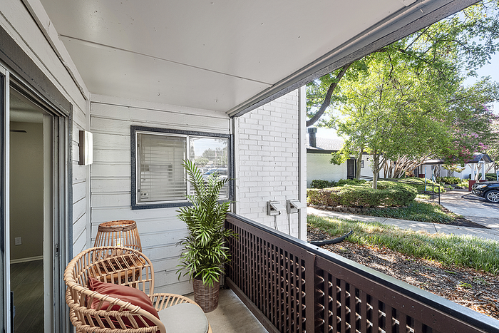 Charming balcony with cozy seating and lush greenery, overlooking a serene garden in a residential setting.