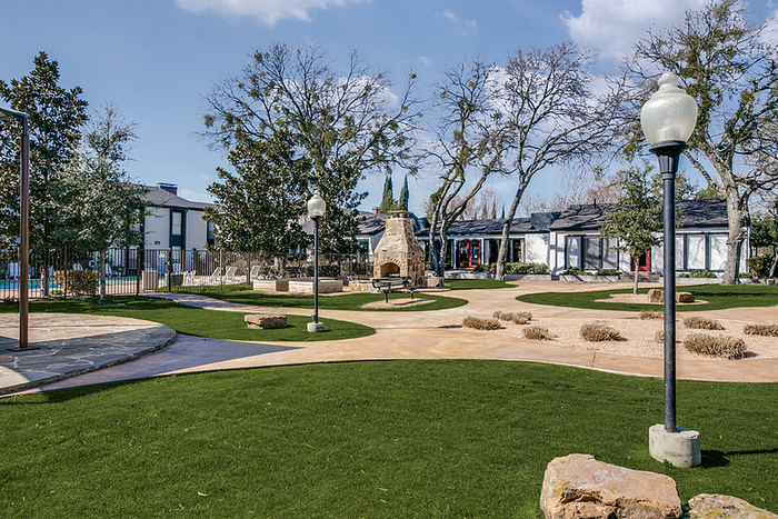 Charming outdoor space with a cozy stone path, lush green lawns, and stylish lighting, surrounded by trees and modern architecture.