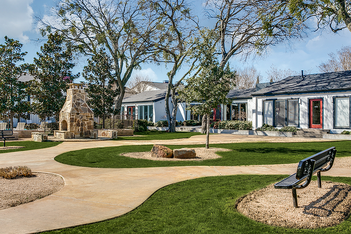 Charming outdoor space with a cozy stone fireplace, lush green lawns, winding pathways, and a serene seating area, perfect for relaxation and enjoyment.