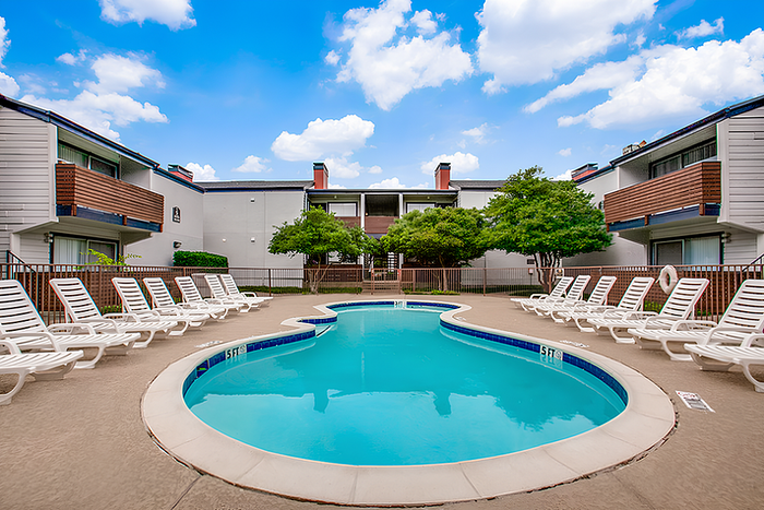 Inviting apartment community pool area with lounge chairs under a clear blue sky.