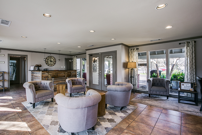 Charming clubhouse with modern decor, featuring cozy gray armchairs, a rustic wooden reception desk, and natural light from large windows, perfect for welcoming guests.