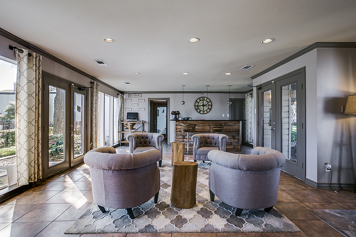 Spacious and inviting clubhouse area with plush armchairs, stylish lighting, and large windows offering a garden view.