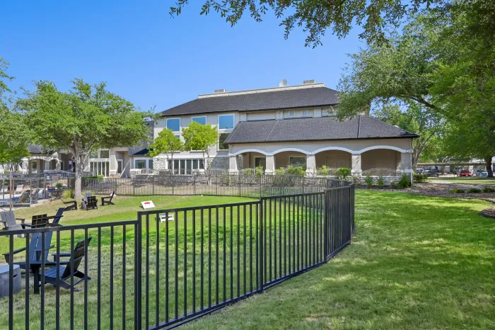 Fenced outdoor lawn and seating area beside the community clubhouse, surrounded by mature trees.