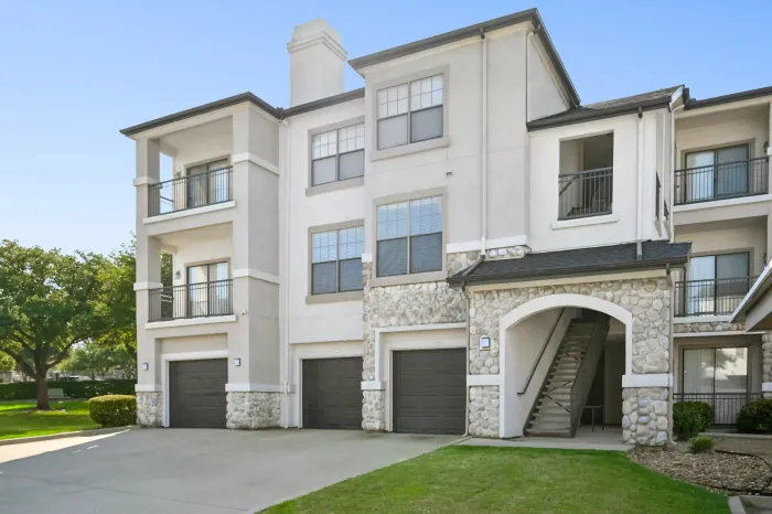 Exterior of a multi-story apartment building featuring private balconies, attached garages, and stone accents.