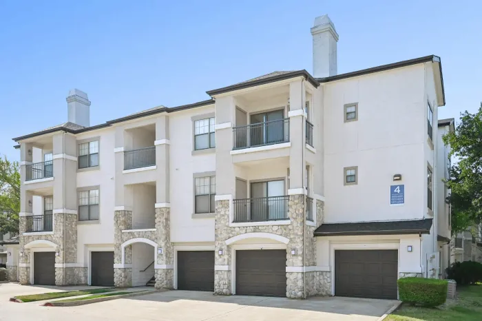 Exterior of a three-story apartment building featuring private balconies, attached garages, and stone accents.
