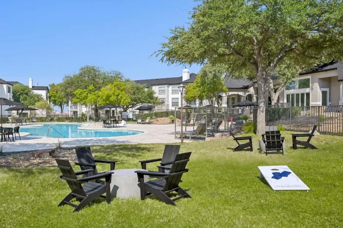 Resort-style swimming pool and outdoor lawn with lounge seating, fire pit chairs, and a cornhole game.