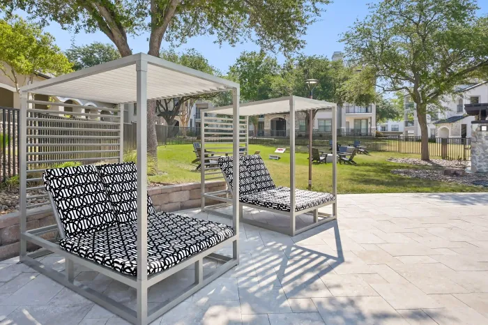 Shaded poolside cabanas with lounge chairs overlooking a landscaped lawn and outdoor seating area.