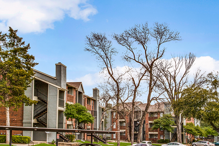 Charming apartment complex with lush greenery and modern architecture set against a clear blue sky.