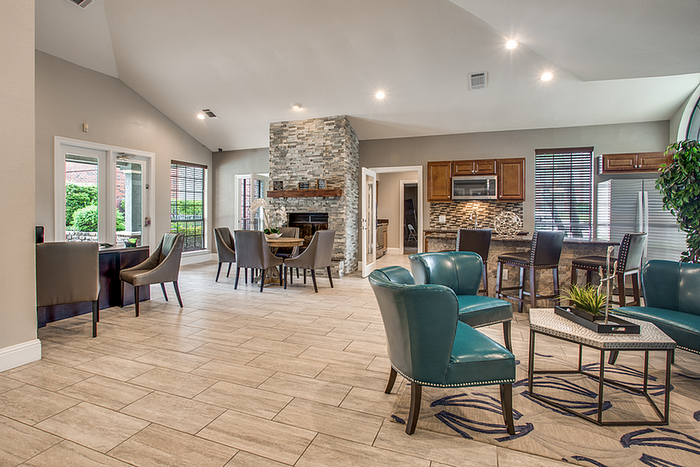 Inviting open-concept clubhouse with modern furnishings, a stone fireplace, and a sleek kitchen in view.