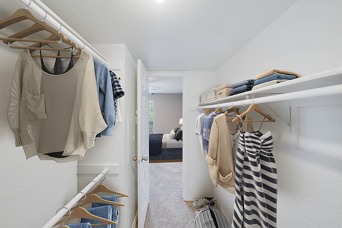 Spacious walk-in closet with ample shelving and stylish clothing, leading to a cozy bedroom with natural lighting.