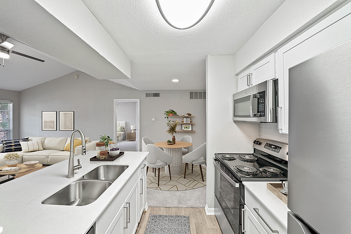 Bright and modern kitchen with sleek stainless steel appliances and open view to a cozy living room and dining area.