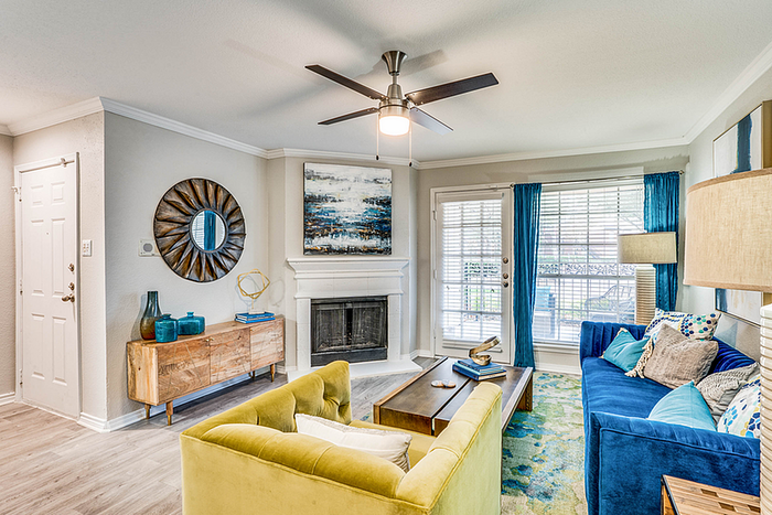 Elegant living room with modern decor, featuring a vibrant blue sofa, a cozy green armchair, and a stylish fireplace. Abundant natural light fills the space through large windows with chic blue curtains.