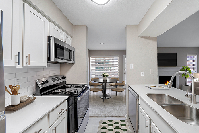 Modern kitchen with sleek white cabinets, stainless steel appliances, and open layout leading to a cozy dining area. Adjacent living space features a warm fireplace, enhancing the inviting atmosphere.