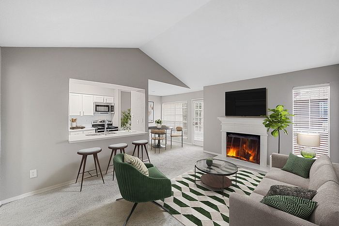 Bright and inviting living room with a cozy fireplace, stylish green accents, and an open view into the modern kitchen.
