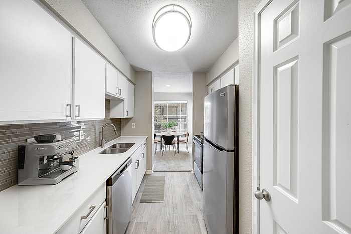 Bright and modern kitchen with sleek white cabinets and stainless steel appliances, leading to a cozy dining area with abundant natural light.