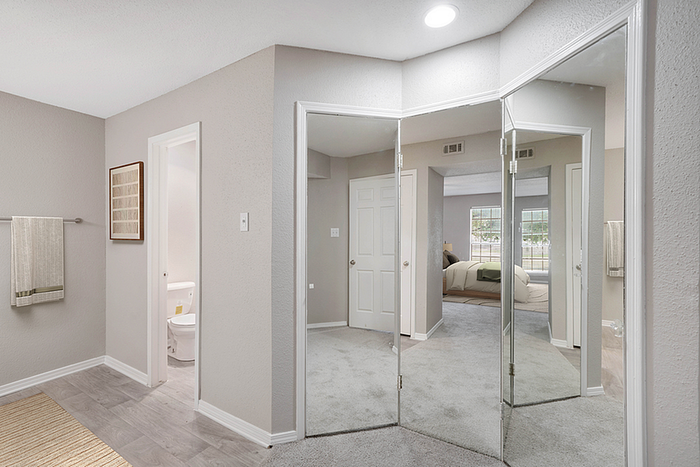 Elegant bedroom and bathroom with modern decor, spacious mirrored closet doors, and inviting natural light.