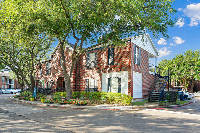 Charming brick apartment building with lush greenery and ample natural light, set in a serene residential neighborhood.
