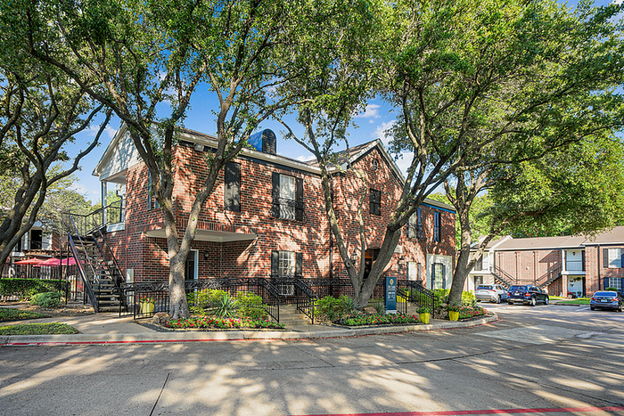 Charming two-story brick apartment building surrounded by lush trees and vibrant landscaping, offering serene living in a vibrant neighborhood.