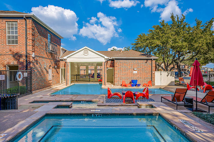 Inviting apartment community with an outdoor pool, vibrant seating area, and lush greenery under a bright blue sky.