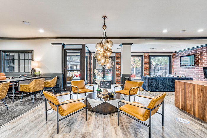 Inviting clubhouse lounge area with modern leather seating, stylish pendant lighting, and a blend of brick and wooden accents, perfect for social gatherings.