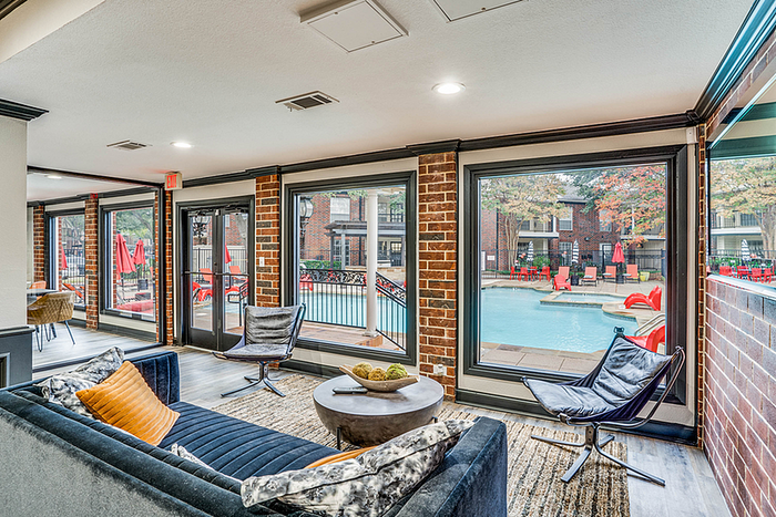 Modern apartment clubhouse with chic seating and large windows showcasing a refreshing pool view with vibrant red umbrellas.