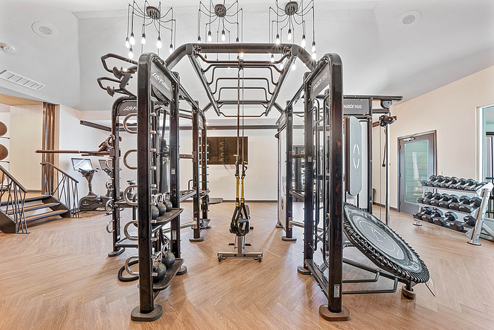 Modern fitness center with state-of-the-art fitness equipment, including kettlebells, multi-station workout rig, exercise bike, and free weights, set in a spacious, stylish room with wooden flooring.