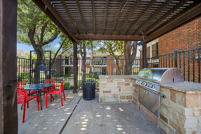 Charming outdoor patio with a modern grill station and vibrant red seating, shaded by a stylish pergola, perfect for entertaining.