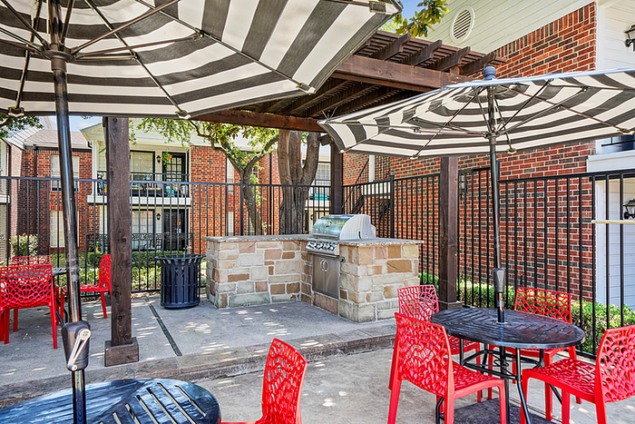 Charming outdoor patio with stylish red chairs, striped umbrellas, and a built-in grill, perfect for entertaining and enjoying sunny days.