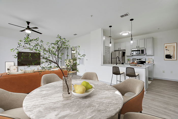 Modern open-plan apartment featuring a chic kitchen with stainless steel appliances, cozy living area with a warm-toned sofa, and a stylish dining space with a marble table and contemporary decor.