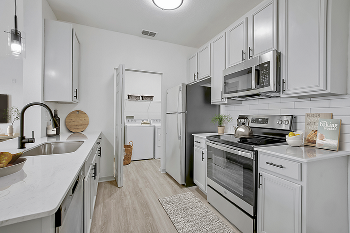 Modern kitchen with sleek white cabinetry, stainless steel appliances, and a convenient adjoining laundry area.