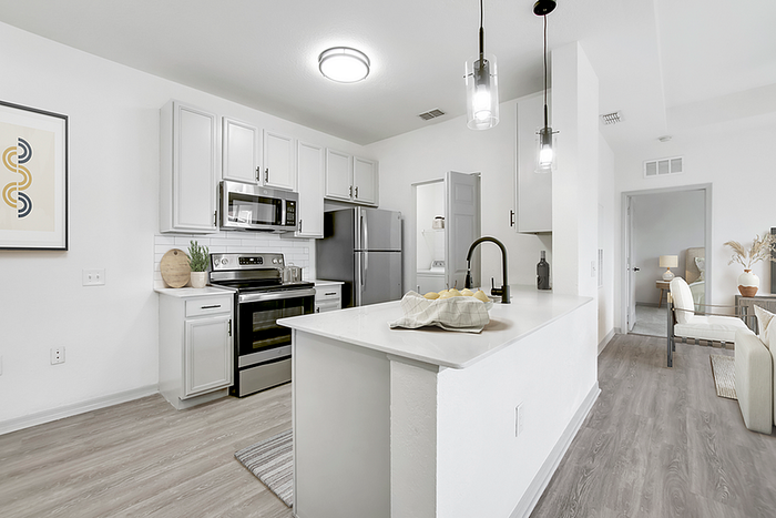 Modern kitchen with sleek appliances, stylish cabinetry, and elegant pendant lighting, leading to a cozy living area with natural decor.