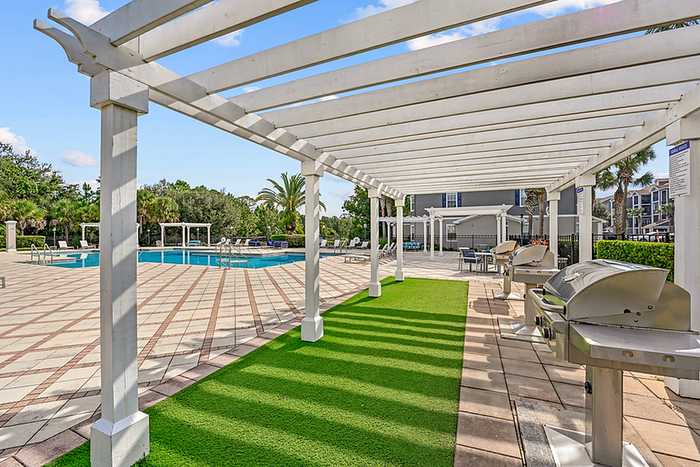 Elegant outdoor space with a stylish pergola, modern grills, and a vibrant pool area surrounded by lush greenery.