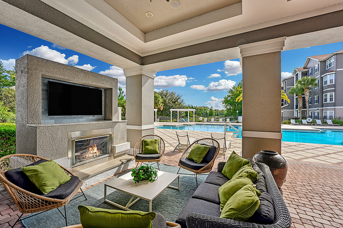 Luxurious poolside lounge featuring a cozy outdoor fireplace, modern seating with green cushions, and a view of a sparkling blue pool under a clear sky.