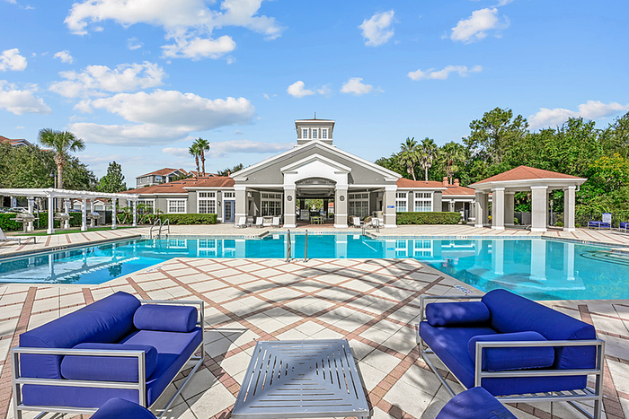 Elegant apartment community showcasing a luxurious pool area with modern lounge chairs, surrounded by lush greenery and a beautiful clubhouse.