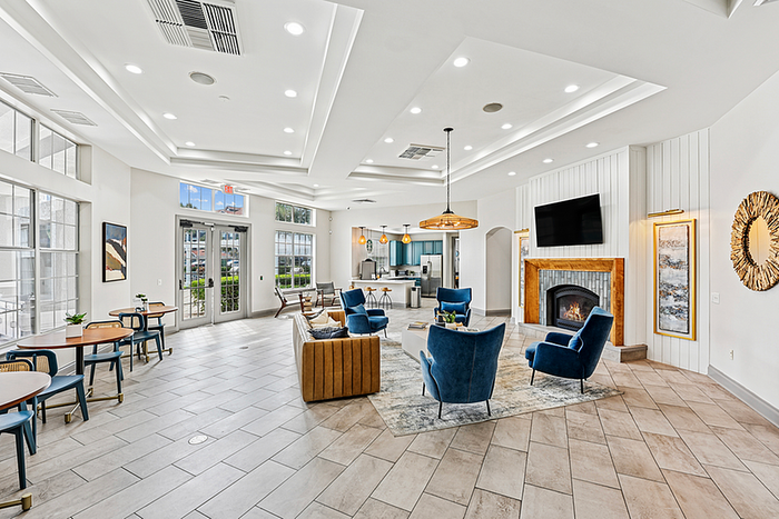 Elegant clubhouse area with contemporary design, featuring plush blue chairs, a cozy fireplace, modern lighting, and ample natural light from large windows.