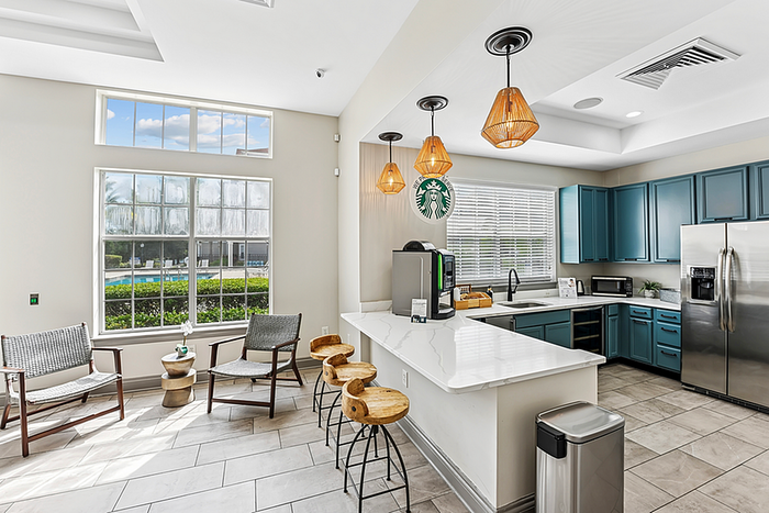 Bright and inviting kitchen space featuring modern teal cabinets, stylish breakfast bar with wooden stools, and large sunlit windows overlooking a serene outdoor view.