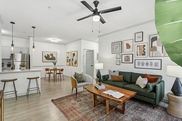 Bright and contemporary living space featuring a cozy green sofa, elegant wooden coffee table, and modern kitchen with stainless steel appliances and pendant lighting.