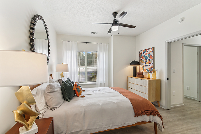 Inviting bedroom with modern decor, featuring a large round mirror, elegant ceiling fan, and warm natural light.