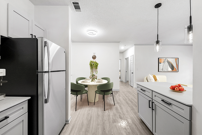 Modern apartment interior showcasing a sleek kitchen with stainless steel appliances, a stylish dining area with green chairs, and a cozy living space in serene neutral tones.