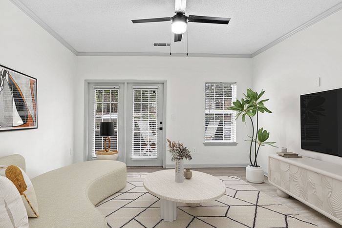 Modern living room with elegant curved sofa, chic ceiling fan, large TV, and abundant natural light through double French doors.