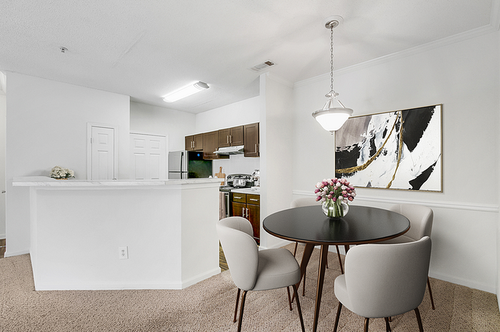 Modern dining area with elegant table and chairs, adjacent to a sleek kitchen with stainless steel appliances and chic artwork.