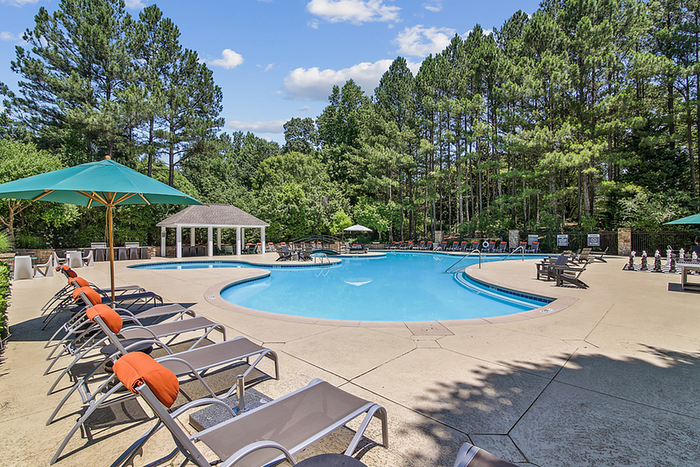 Luxurious outdoor pool surrounded by lush greenery and stylish lounge chairs under umbrellas, perfect for relaxation and leisure.