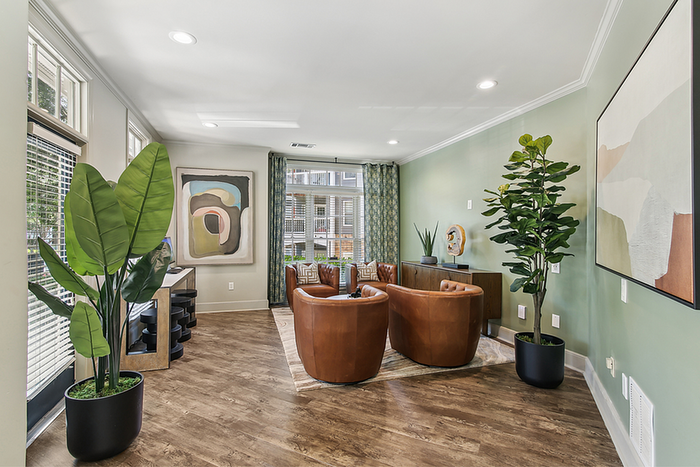 Bright and stylish clubhouse with modern decor, featuring elegant green walls, chic leather chairs, large potted plants, and abstract art pieces.
