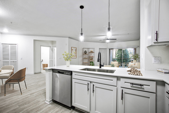 Elegant open-concept kitchen and living area with modern finishes, stylish lighting, and large windows offering a view of lush greenery.