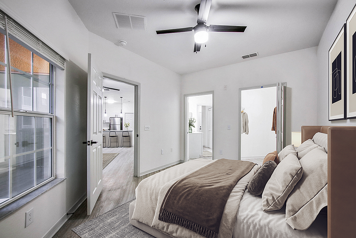Modern and inviting bedroom with plush bedding and artwork, leading to an open kitchen area with sleek finishes.
