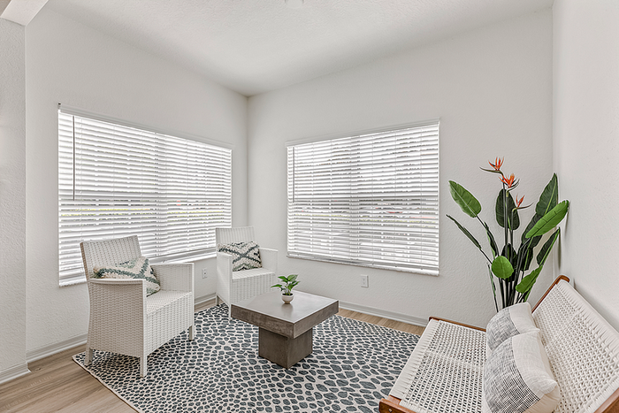 Bright and inviting sunlit corner room with cozy white wicker furniture, elegant decor, and vibrant plants creating a relaxing oasis.