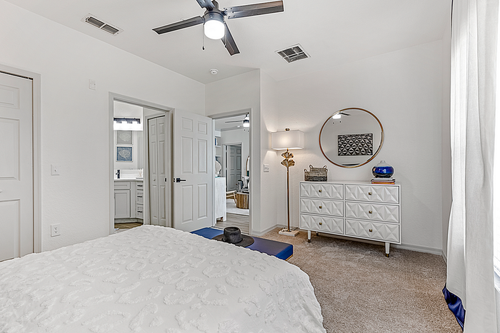 Elegant bedroom showcasing a plush bed, modern ceiling fan, stylish dresser with a round mirror, and soft natural light.